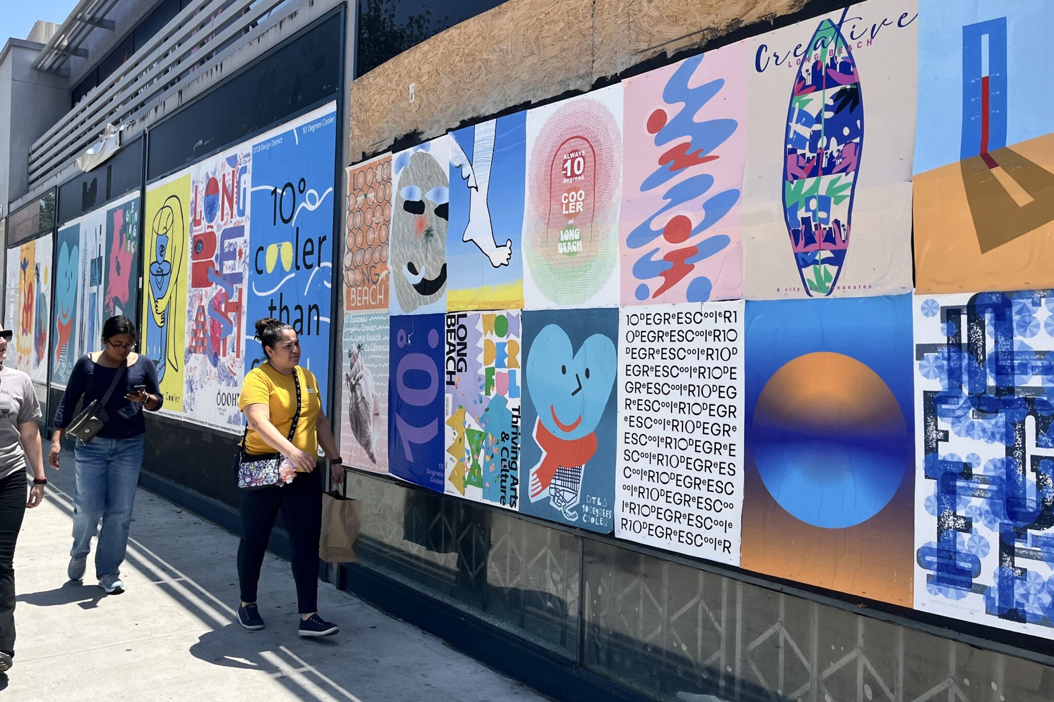 Person walks past colorful street art panels on a sunny day.